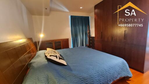 Spacious bedroom with a large bed, wooden cupboard, and a window with blue curtains.