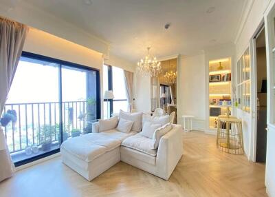 Bright living room with large windows, balcony access, plush sofa, chandelier, and built-in shelving