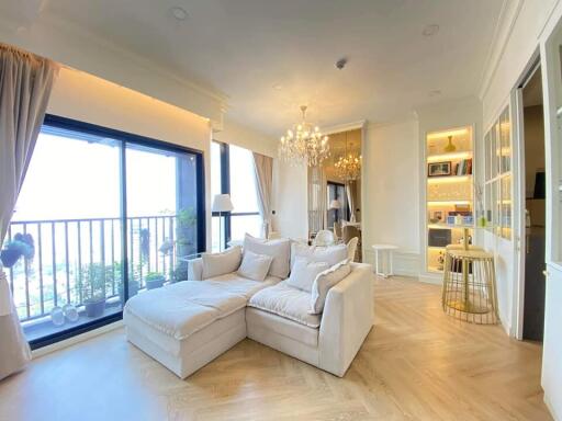 Bright living room with large windows, balcony access, plush sofa, chandelier, and built-in shelving