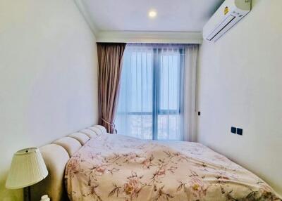 A well-lit bedroom with wall-mounted air conditioning and a large window with sheer curtains.