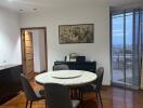 Dining area with a round table and chairs, partial view of another room, large window with a city view