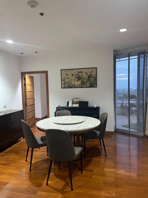 Dining area with a round table and chairs, partial view of another room, large window with a city view