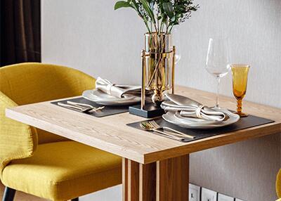 Cozy dining area with a wooden table set for two with yellow chairs, decorated with a flower vase