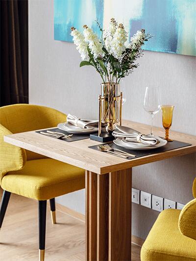 Cozy dining area with a wooden table set for two with yellow chairs, decorated with a flower vase