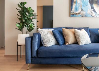 Modern living room with blue sofa, cushions, indoor plant, and wall art