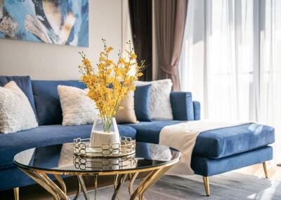 Modern living room with blue sofa, decorative pillows, glass coffee table, and natural light