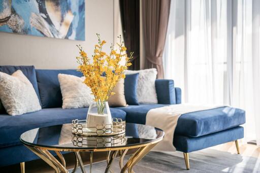 Modern living room with blue sofa, decorative pillows, glass coffee table, and natural light