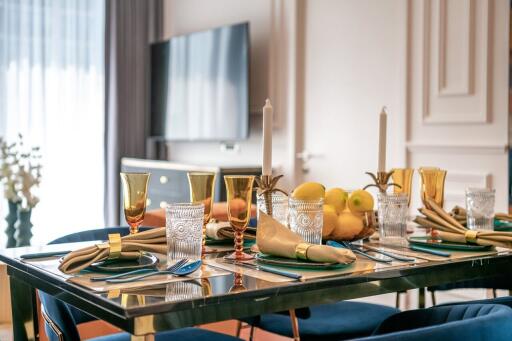 Elegant dining room with a well-set table, golden utensils and a modern TV in the background