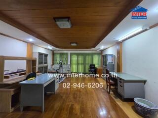 Office space with multiple desks and chairs, featuring a wooden floor and ceiling with overhead lights