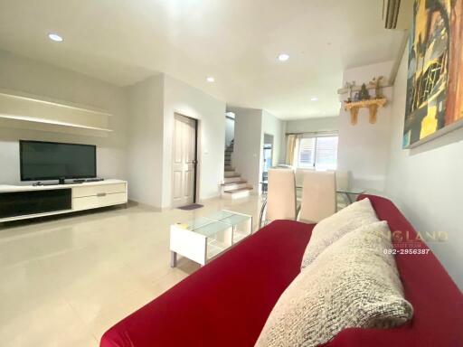 Modern living room with a wall-mounted TV, red sofa, and dining area