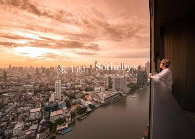 Person standing on a balcony overlooking a cityscape at sunset