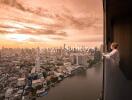 Person standing on a balcony overlooking a cityscape at sunset