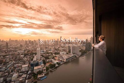 Person standing on a balcony overlooking a cityscape at sunset