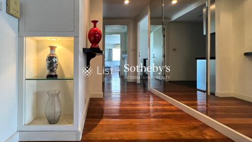 Well-lit hallway with decorative vases, wooden flooring, mirror wall, and built-in shelves