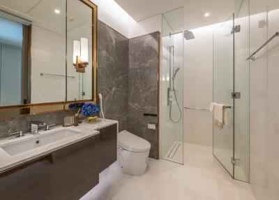 Modern bathroom with glass shower, toilet, and double sink