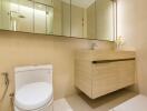 Modern bathroom with beige walls, a toilet, a floating sink cabinet, and a large mirror