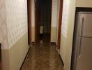 A well-lit hallway with tiled flooring and a refrigerator.