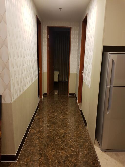 A well-lit hallway with tiled flooring and a refrigerator.