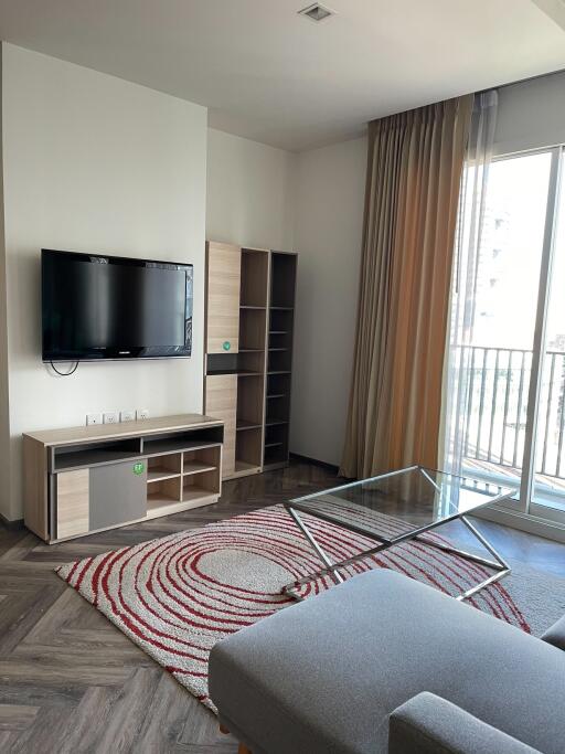 Modern living room with TV, shelving unit, glass coffee table, and large window