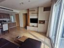 Modern living room with TV and wooden furniture, adjacent to an open kitchen.