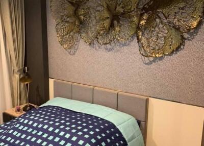 Photo of a bedroom with a modern design, featuring a bed with patterned bedding, wall art above the headboard, and a bedside table with a lamp