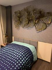 Photo of a bedroom with a modern design, featuring a bed with patterned bedding, wall art above the headboard, and a bedside table with a lamp