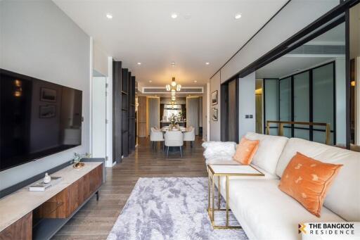 Modern living room with large TV, beige sofa, and dining area in the background