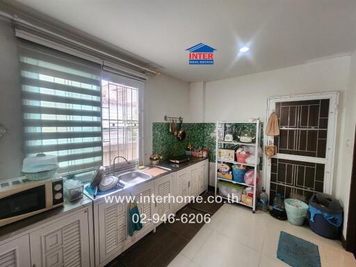 Modern kitchen with green tile backsplash, metal sink, and storage shelves.