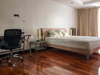 Spacious bedroom with wooden flooring, a desk, and natural lighting from a large window