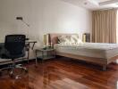 Spacious bedroom with wooden flooring, a desk, and natural lighting from a large window