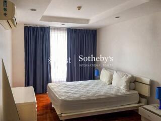 Minimalist bedroom with blue curtains, white bedding, and air conditioning unit