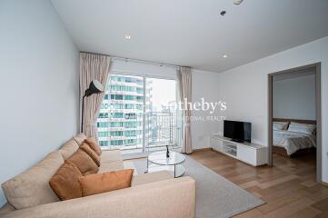 Living room with a beige sofa, wall-mounted TV, a window with a city view, and an adjacent bedroom