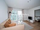 Living room with a beige sofa, wall-mounted TV, a window with a city view, and an adjacent bedroom