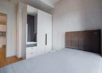 Modern bedroom with a large bed, white wardrobe, and view into the kitchen