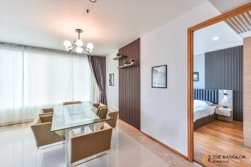 Modern dining area with glass table and six chairs, view into a modern bedroom