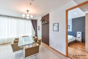 Modern dining area with glass table and upholstered chairs, adjacent to a cozy bedroom.