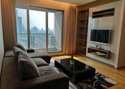 Modern living room with a city view, large sofa, flat-screen TV, and balcony access