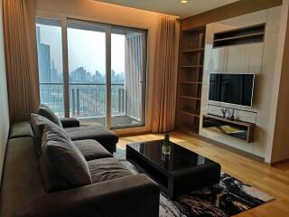 Modern living room with a city view, large sofa, flat-screen TV, and balcony access