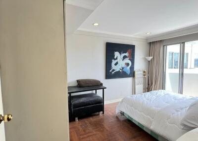 Spacious bedroom with a large window, modern artwork, and wooden floors