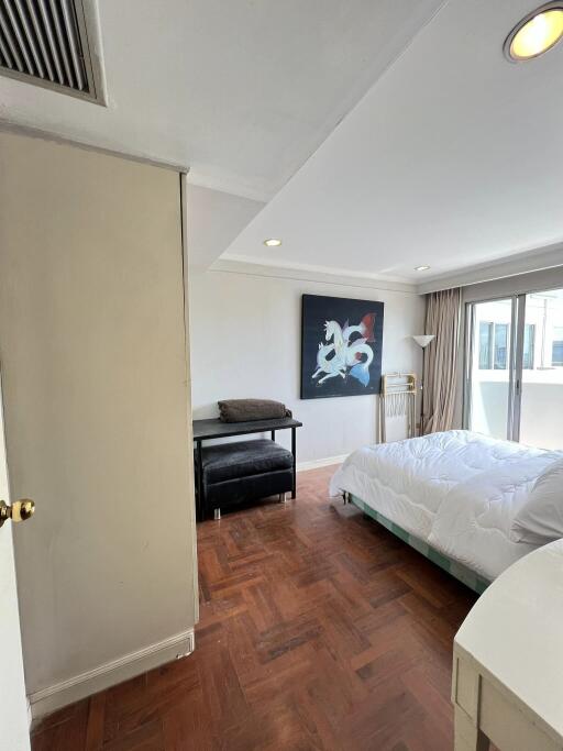 Spacious bedroom with a large window, modern artwork, and wooden floors