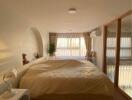 Cozy bedroom with a large bed, nightstand, and natural light through large windows