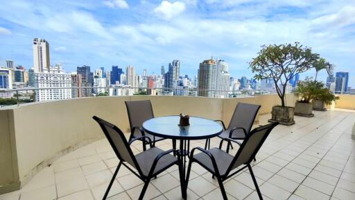 View of city skyline from a spacious balcony with a round glass table and four chairs