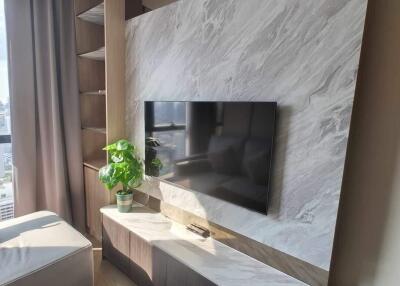 A modern living room with a wall-mounted TV, built-in shelves, and a potted plant on a marble surface.