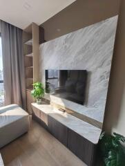 A modern living room with a wall-mounted TV, built-in shelves, and a potted plant on a marble surface.