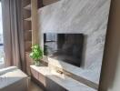 A modern living room with a wall-mounted TV, built-in shelves, and a potted plant on a marble surface.