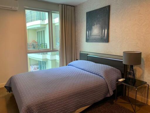 A cozy bedroom with a large window, a bed, and a nightstand with a lamp