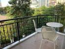 A cozy balcony with a small table and two chairs, overlooking a green area and city buildings.