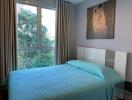 Well-lit bedroom with a large window, teal bedspread, and artwork on the wall