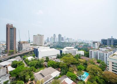 View of cityscape from above with various buildings, trees, and construction cranes