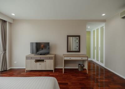 Modern bedroom with wooden flooring, a TV on a stand, a dressing table with a mirror, and a large wardrobe